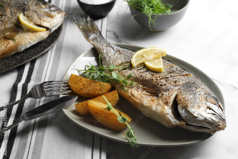 Seafood. Delicious baked fish served with lemon, potato and microgreens on light table, closeup Seafood. Delicious baked fish served with lemon, potato and microgreens on light table, closeup