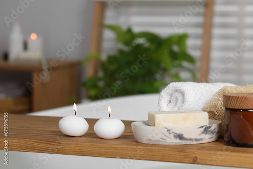 Wooden board with spa products and burning candles on bath tub in bathroom, space for text