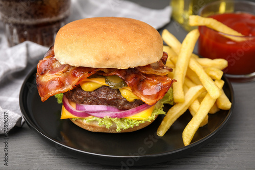 Tasty burger with bacon, vegetables and patty served with french fries on grey wooden table, closeup