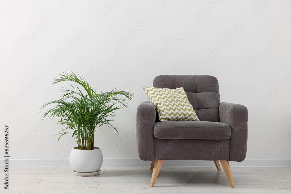 Comfortable armchair with cushion and houseplant near white wall indoors. Interior design