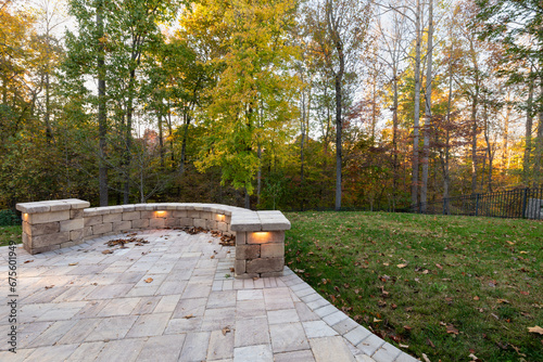 Picturesque backyard view in autumn season with patio pavers and stone wall, autumn leaves, and colorful woods in the background