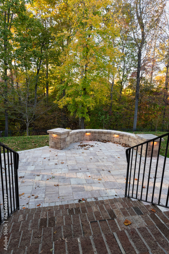 Picturesque backyard view in autumn season with patio pavers and stone wall, autumn leaves, and colorful woods in the background