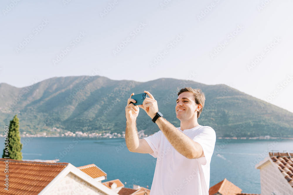 Smiling guy takes pictures of landscapes with a smartphone on an observation deck over the sea