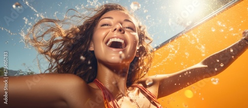 In the background of a summer pool party a young adult woman with an orange in her hand opens a can of energy drink the metallic pop echoing over the sound of splashing water as bubbles tan photo