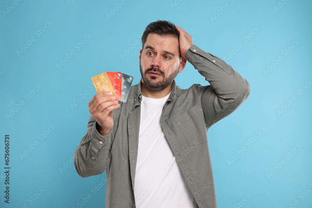 Confused man with credit cards on light blue background. Debt problem Confused man with credit cards on light blue background. Debt problem