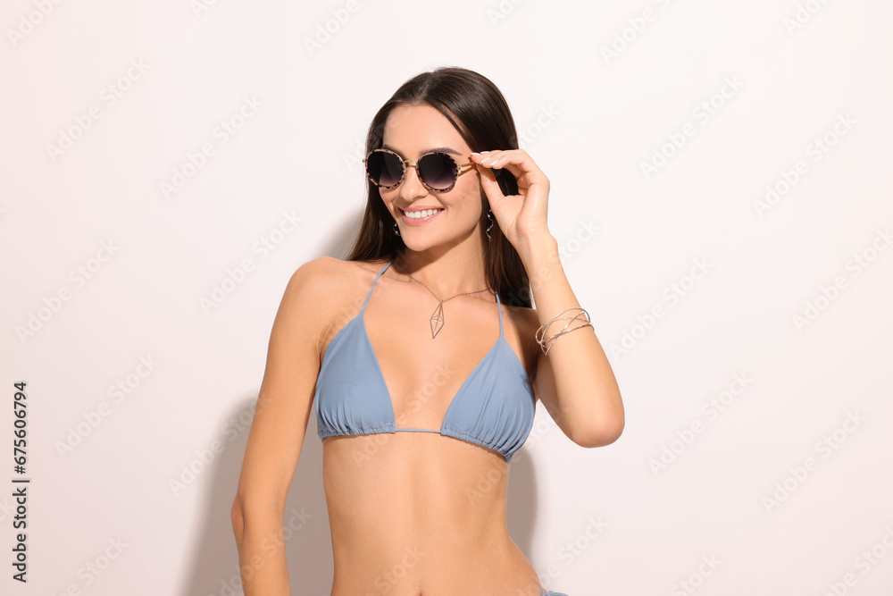 Young woman in stylish bikini and sunglasses on white background