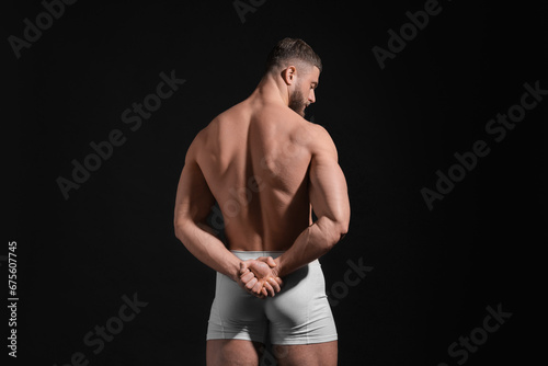 Young man in stylish white underwear on black background, back view