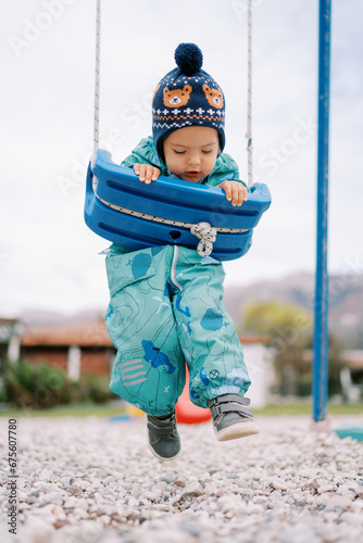 Little girl hangs on her stomach on a swing and dangles her legs