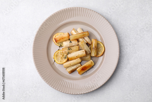 Plate with baked salsify roots, lemon and thyme on light grey table, top view
