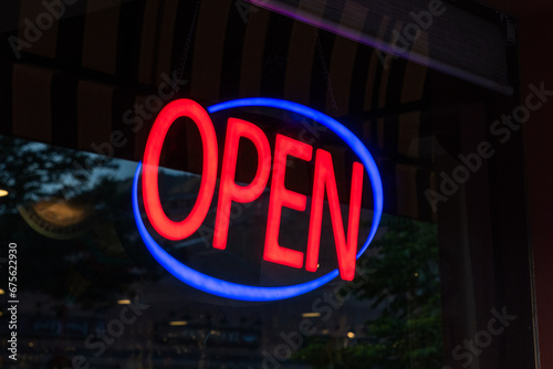 An open sign glows in the front window of a shop.