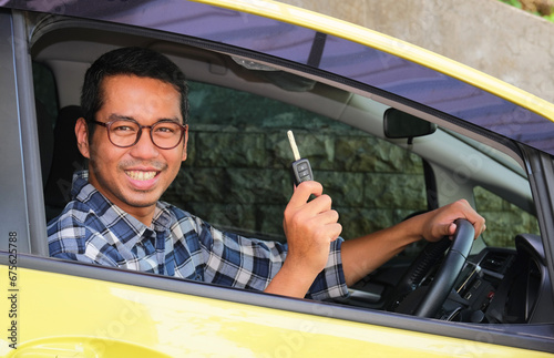 Adult Asian man smiling happy from inside a car while showing the key