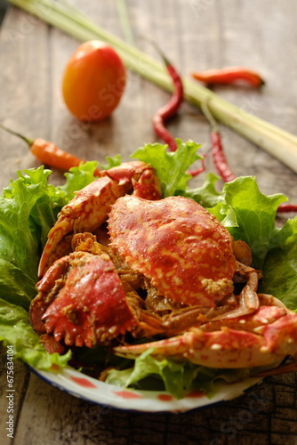 Rajungan Asam Manis, the crab is a popular seafood dish in the coastal area. The crab is served with tomato sauce, chili, lemongrass, lettuce and spices. Served on wooden table. Indonesian food. photo