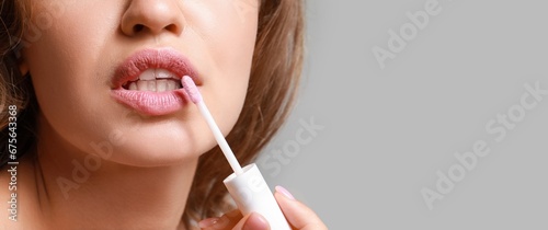 Beautiful woman applying lipstick against grey background with space for text, closeup