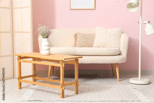 Light wooden coffee table with sofa, dressing screen and floor lamp near pink wall