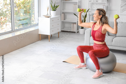 Beautiful adult woman exercising with dumbbells on fitness ball at home