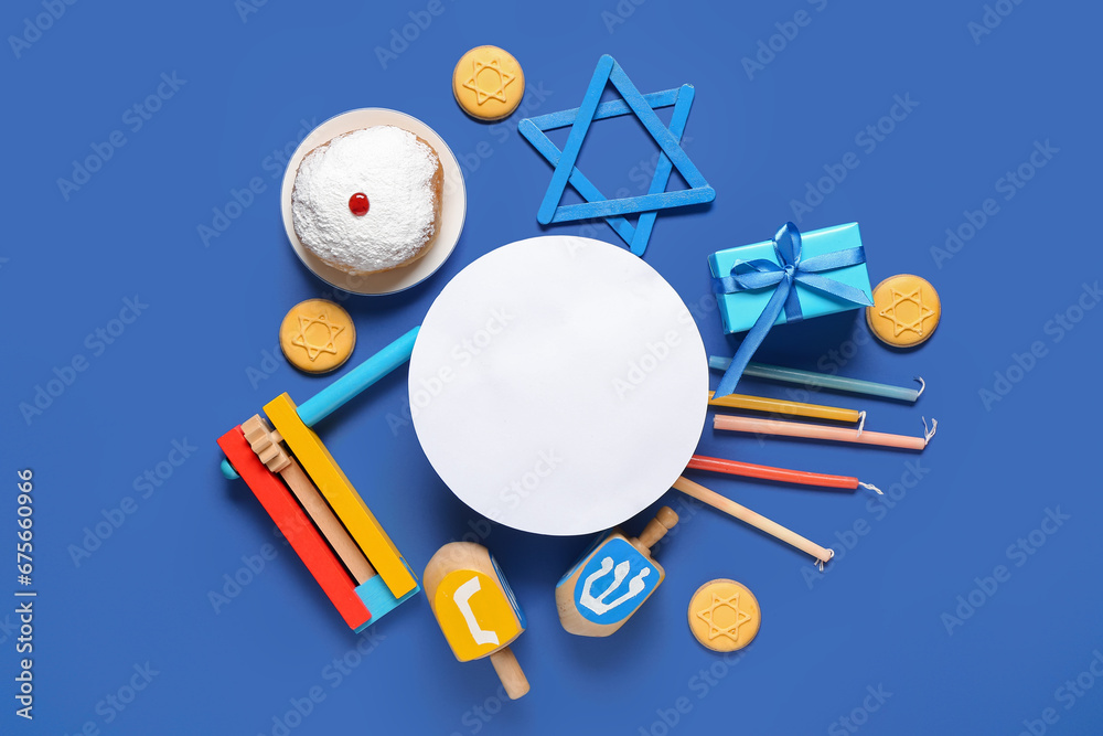Hannukah composition with blank greeting card, candles, dreidels, gift box and donut on blue background