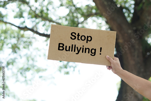 Close up hand holds paper placard with text Stop Bullying, outdoor background.  Concept, campaign for calling everybody to stop bullying each other by using bad word, action, texting or online.     © Sanhanat