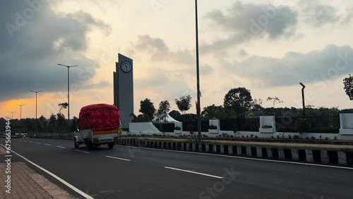 Monument with clock on Asian Avenue during sunset, shuttle passing by, India. photo