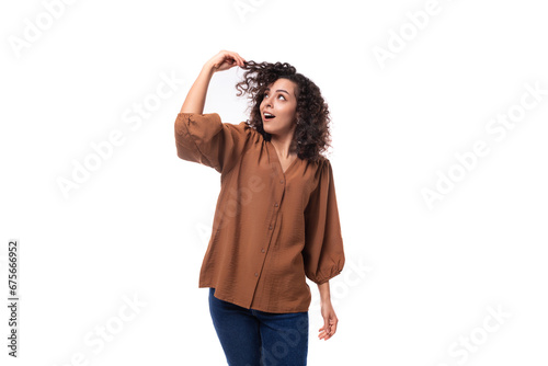 young positive cheerful slender woman with curls dressed in a brown blouse touches her hair