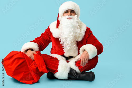 Santa Claus with bag of gifts sitting on blue background