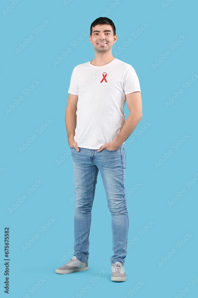 Fototapeta premium Handsome young man with red ribbon on blue background. World AIDS day concept