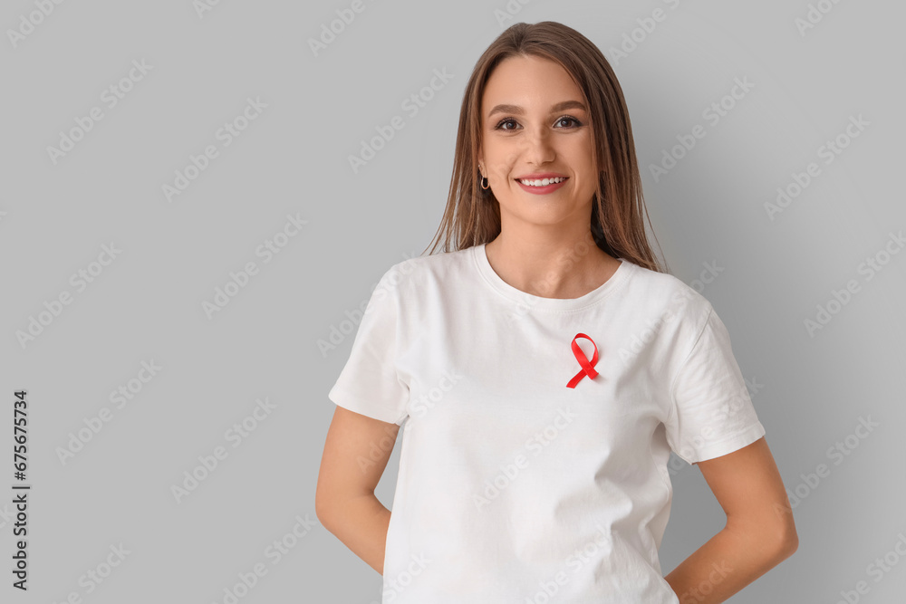 Obraz premium Pretty young woman with red ribbon on grey background. World AIDS day concept