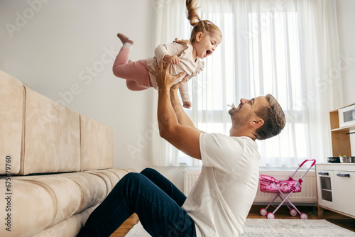 Father is playing with his daughter at home and tossing her in the air.
