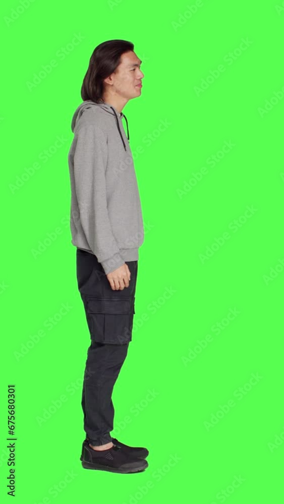 Profile of asian man asking person to come over, encouraging people to get closer while he is standing against full body greenscreen. Adult in casual clothes urging someone to approach him. Profile of asian man asking person to come over, encouraging people to get closer while he is standing against full body greenscreen. Adult in casual clothes urging someone to approach him.