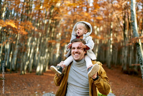 Little girl sits on the shoulders of her father holding her hands to his face