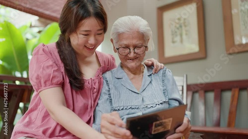 Asian grandmother and young granddaugther looking through a family photo album together while leisure time at home. Family moments and memory of life. Family Relationship concept photo