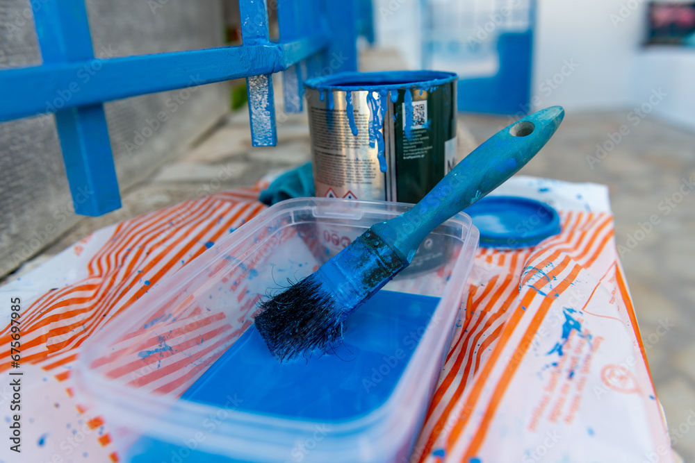 Painting a metal fence with a tin of blue paint and paint brush. Home improvements.
