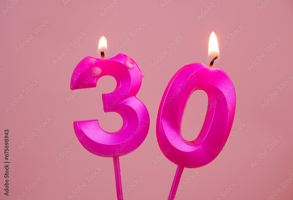 Pink birthday candles burning on pink background. Number 30.
