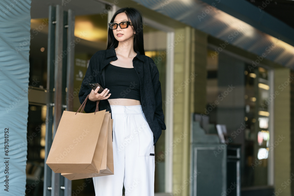 Young woman standing along the road holding shopping bags and using mobile phone. Purchases, black friday, discounts Young woman standing along the road holding shopping bags and using mobile phone. Purchases, black friday, discounts