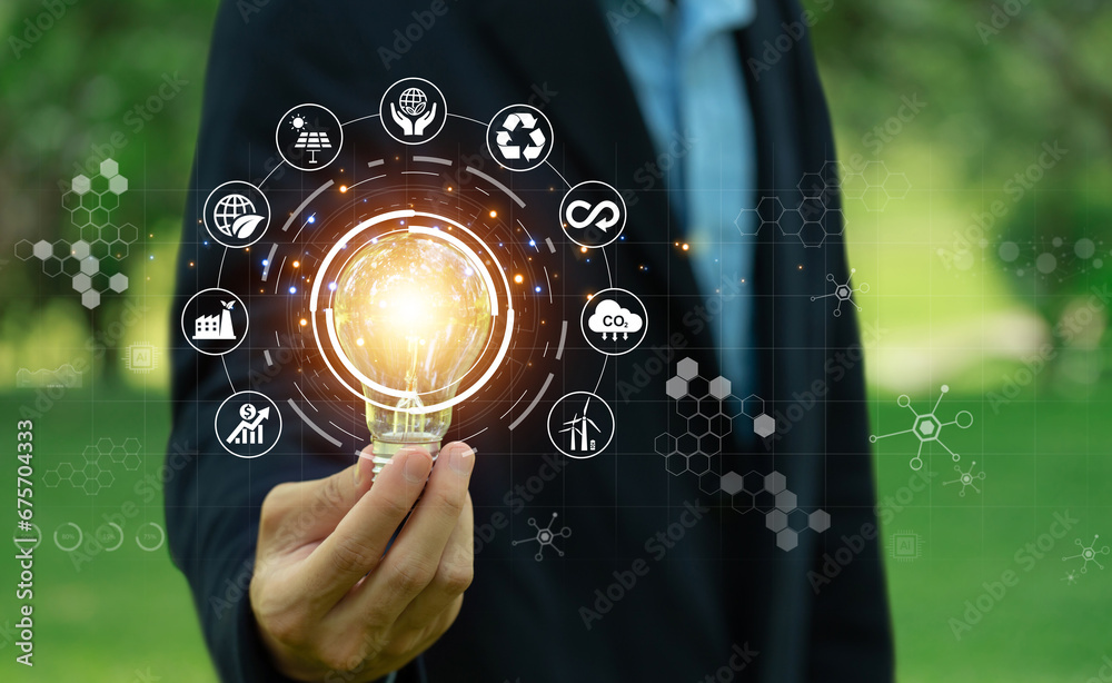 Environmental protection, renewable, sustainable energy sources.businessman holding light bulb against nature on a green background with energy source icons, sustainable development, ESG, Ecology - obrazy, fototapety, plakaty 