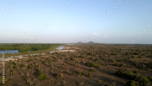 Drone moving above a vast expand of land revealing a big body of water on the left side, two mountains in the horizon, as this beautiful grassland in Porlamar, Margarita Island, Venezuela. photo