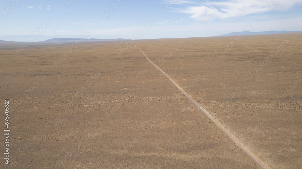 A white SUV is driving fast on a dusty road in the steppe. Clouds of dust fly from under the wheels and from the roof of the car. The jeep easily passes a dirt road. Blue sky and white clouds. A white SUV is driving fast on a dusty road in the steppe. Clouds of dust fly from under the wheels and from the roof of the car. The jeep easily passes a dirt road. Blue sky and white clouds.