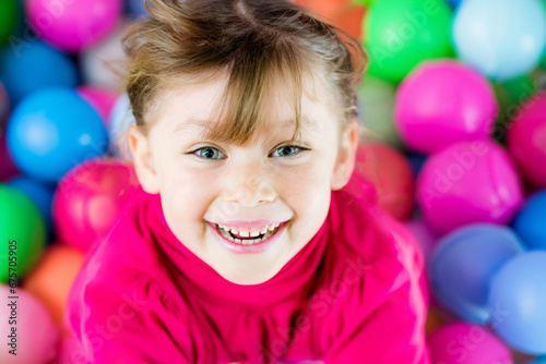 Portrait of a cute happy little girl playing in a colorful plastic ball park 