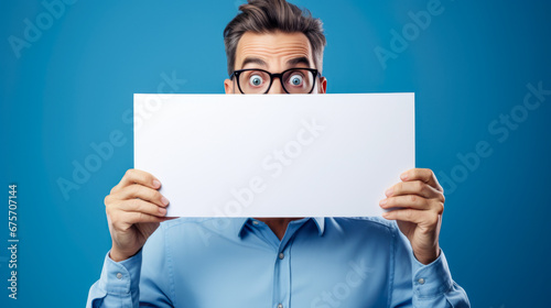 Man holding a blank sign during surprised expression on blue background.