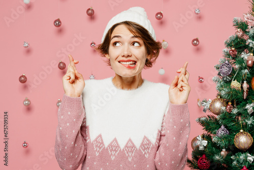 Cuadro en lienzo Merry young woman wear white sweater hat posing wait special moment, keep fingers crossed, making wish isolated on plain pastel pink background