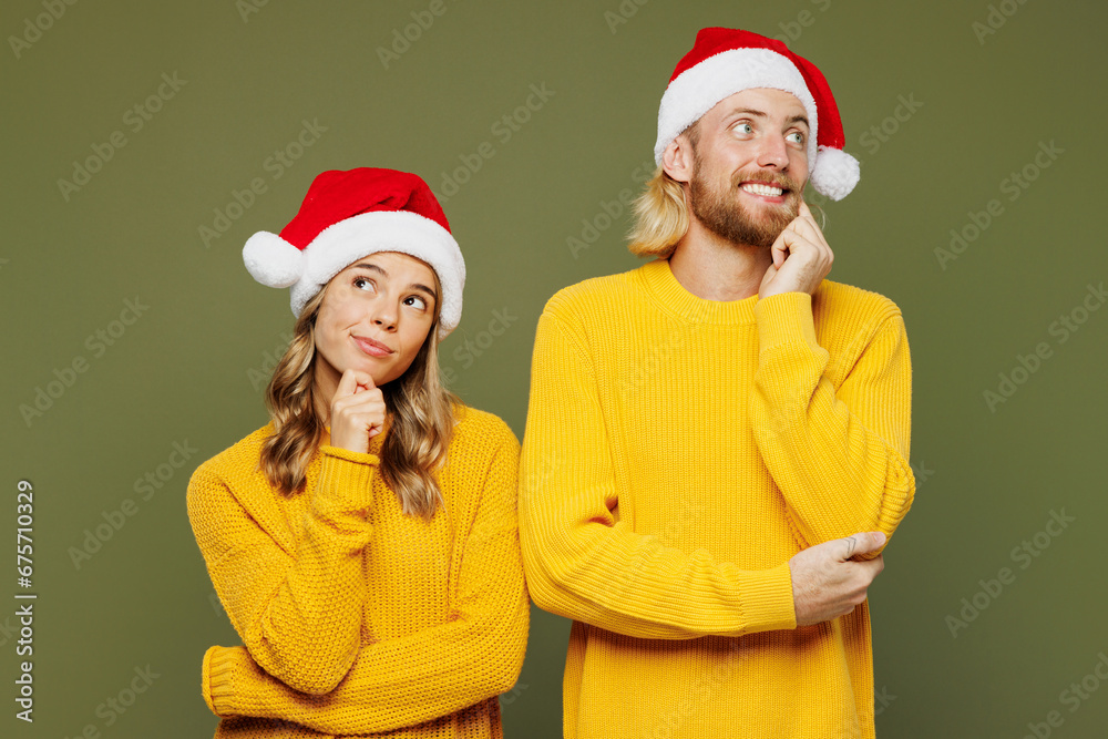 Merry young couple two friends man woman wear sweater Santa hat posing put hand prop up on chin, lost in thought and conjectures isolated on plain green background. Happy New Year Christmas concept. Merry young couple two friends man woman wear sweater Santa hat posing put hand prop up on chin, lost in thought and conjectures isolated on plain green background. Happy New Year Christmas concept.