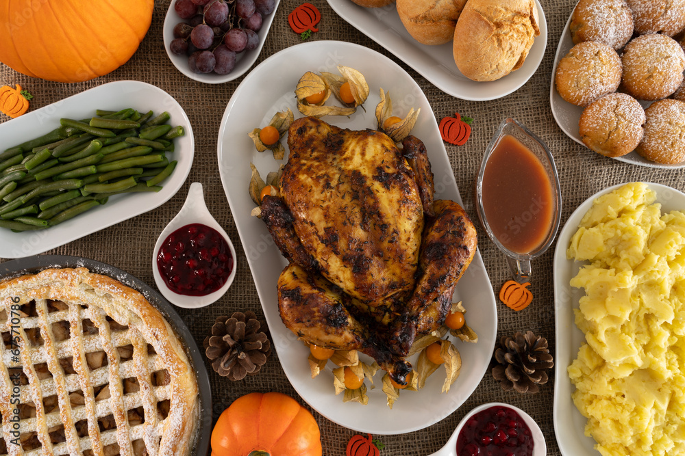 Thanksgiving day dinner table with roasted chicken or turkey, mashed potatoes, cranberry sauce, gravy, apple pie and other holiday season foods. Traditional autumn fall feast flat lay composition. Thanksgiving day dinner table with roasted chicken or turkey, mashed potatoes, cranberry sauce, gravy, apple pie and other holiday season foods. Traditional autumn fall feast flat lay composition.