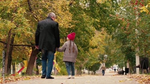 Positive father with little daughter walk along road in autumn city park