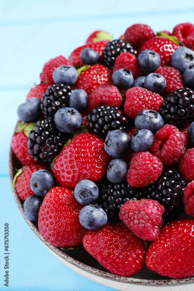Different fresh ripe berries in bowl on light blue table, closeup Different fresh ripe berries in bowl on light blue table, closeup
