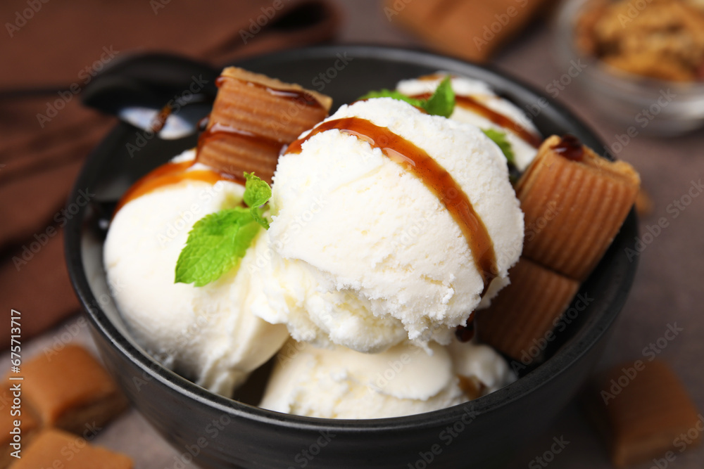 Bowl of tasty ice cream with caramel sauce, candies and mint on table, closeup Bowl of tasty ice cream with caramel sauce, candies and mint on table, closeup