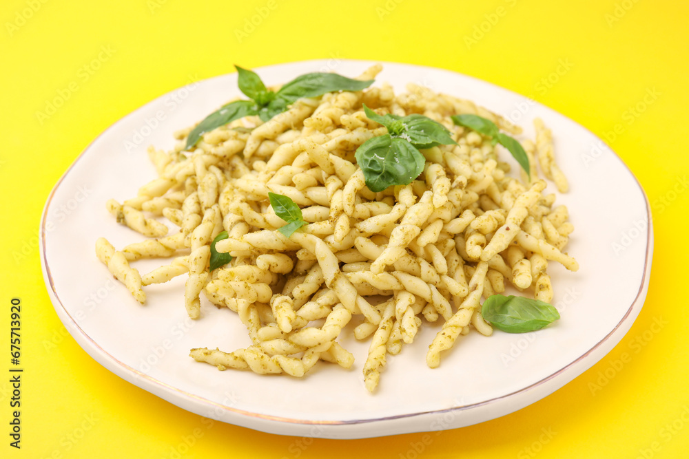 Plate of delicious trofie pasta with pesto sauce and basil leaves on yellow background