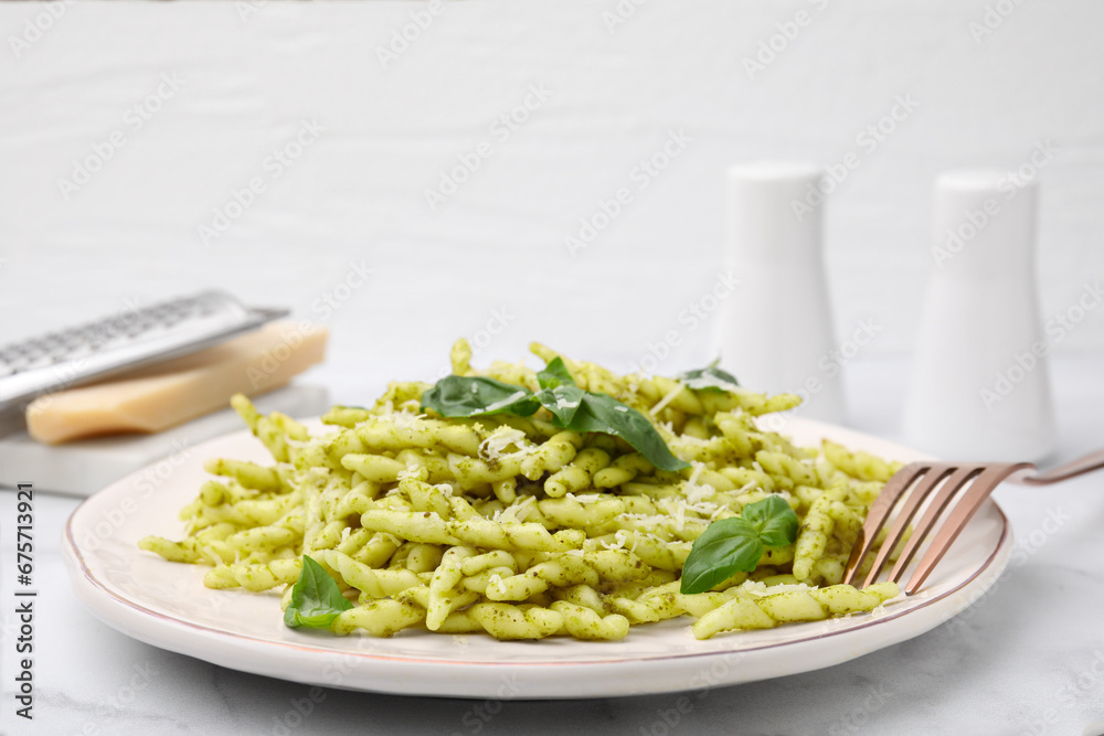 Plate of delicious trofie pasta with pesto sauce, cheese and basil leaves on white marble table