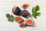 Whole and cut ripe figs with leaves on white wooden table, flat lay