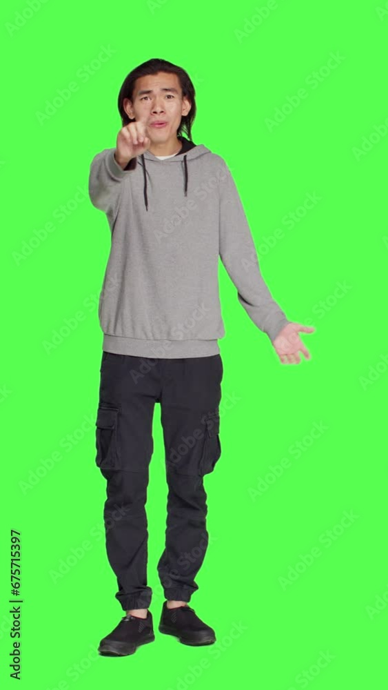 Front view of young adult showing no symbol in studio, expressing negativity and disagreement over isolated greenscreen backdrop. Asian male person being disappointed and disapproving with something. Front view of young adult showing no symbol in studio, expressing negativity and disagreement over isolated greenscreen backdrop. Asian male person being disappointed and disapproving with something.