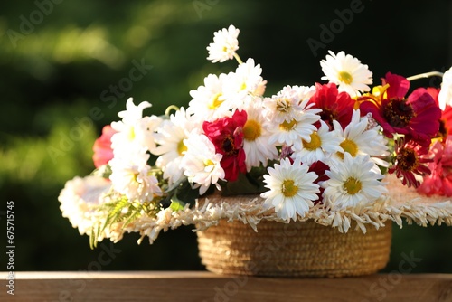Beautiful wild flowers in wicker basket on wooden table against blurred background