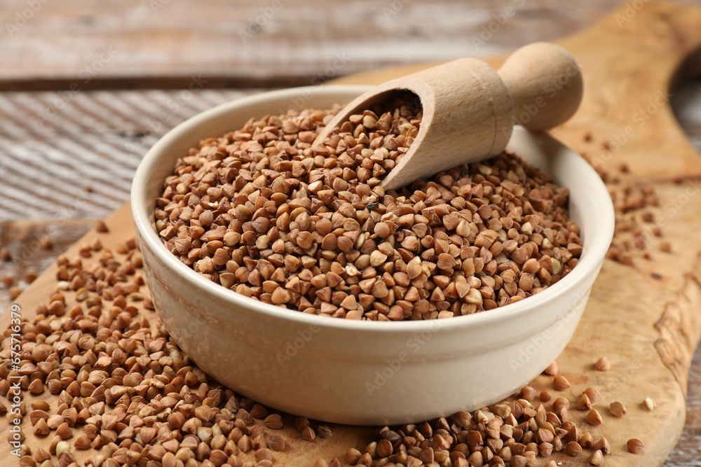 Bowl and scoop with dry buckwheat on wooden table, closeup Bowl and scoop with dry buckwheat on wooden table, closeup